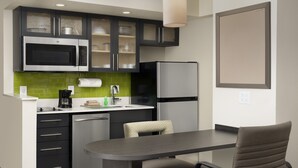 A compact kitchen with a microwave, refrigerator, and a dining area with a table and chairs. - Candlewood Suites Alexandria West by IHG (Alexandria)