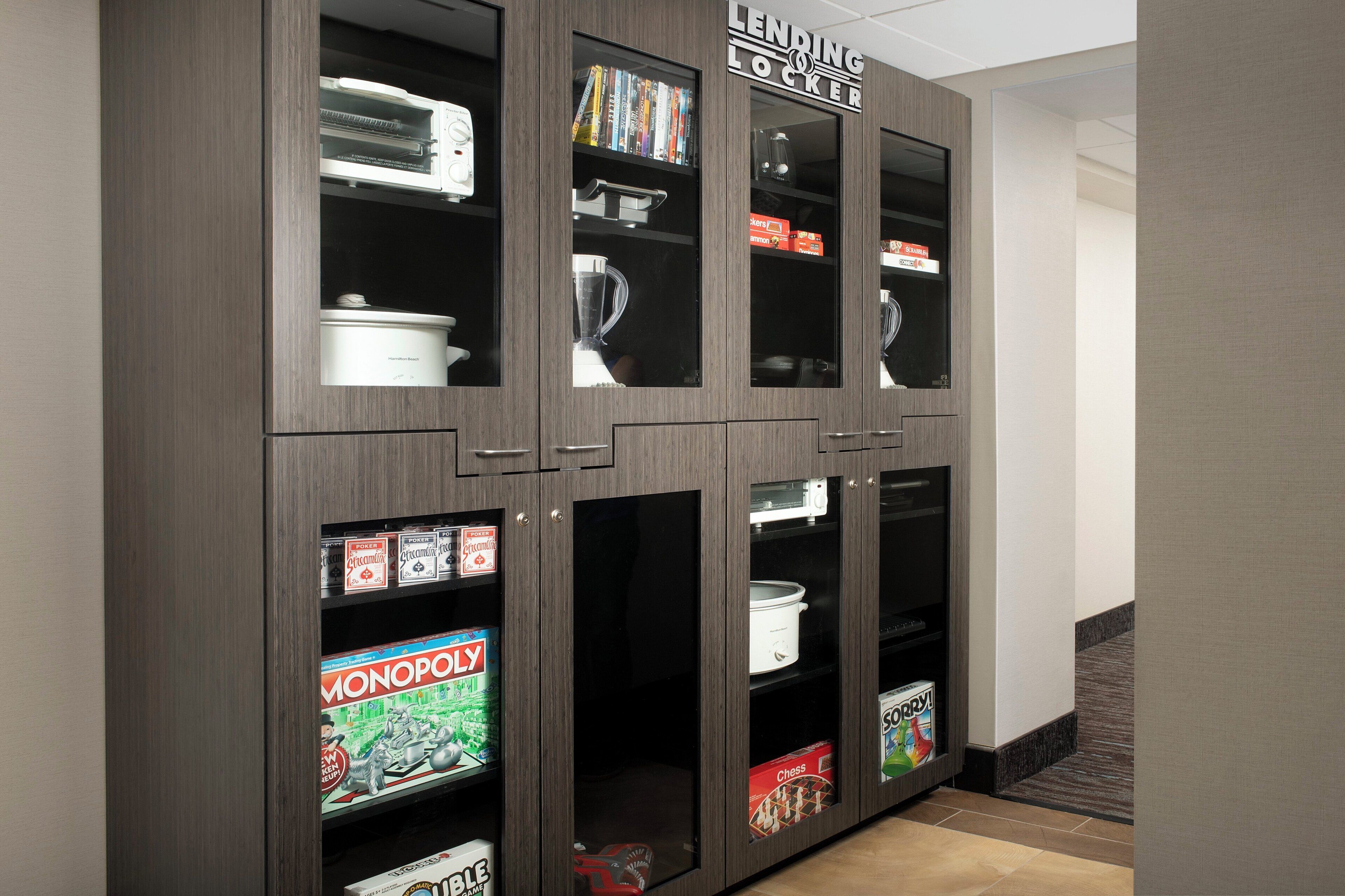 A wooden cabinet with multiple glass-fronted shelves containing kitchen appliances and board games.