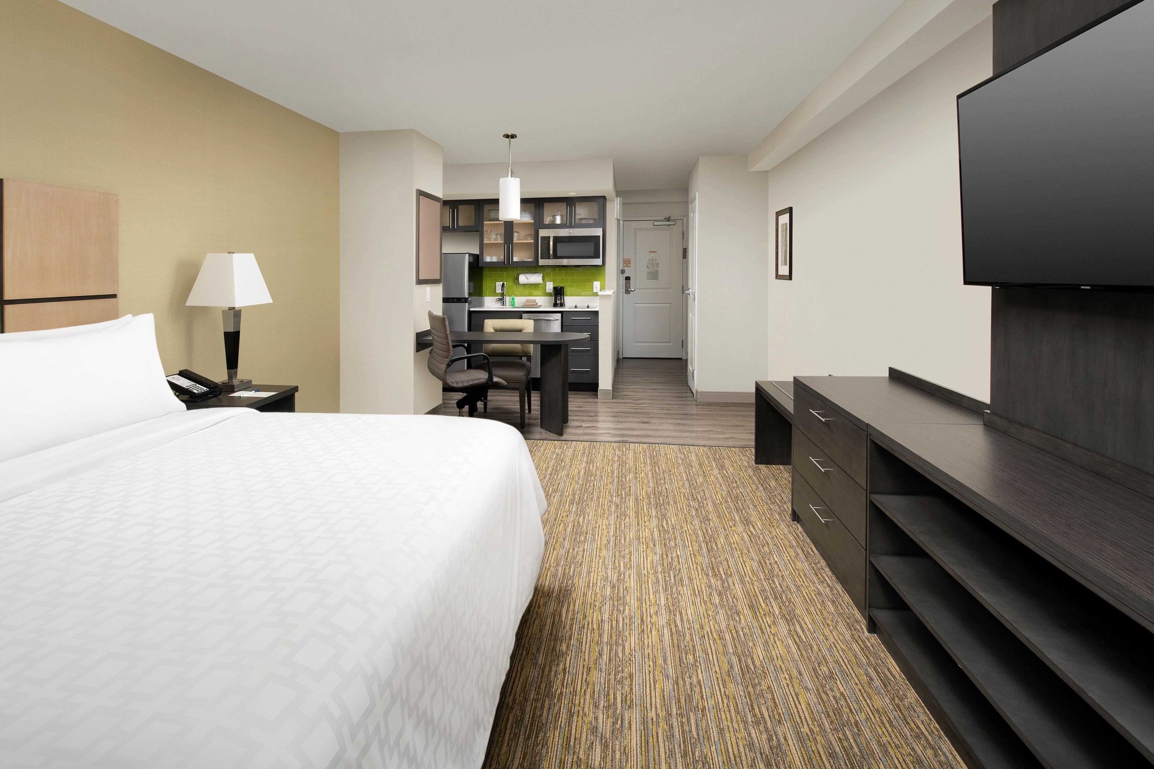 A hotel room with a bed, a desk, a kitchenette, and a TV.