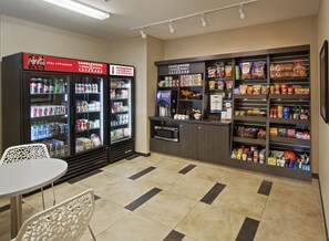 A self-service kiosk with refrigerated beverage dispensers, a microwave, and a variety of snacks and condiments.