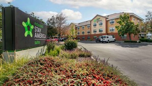 Een Stay America hotel met een bord, parkeerplaats en een gebouw met meerdere ramen en balkons.
