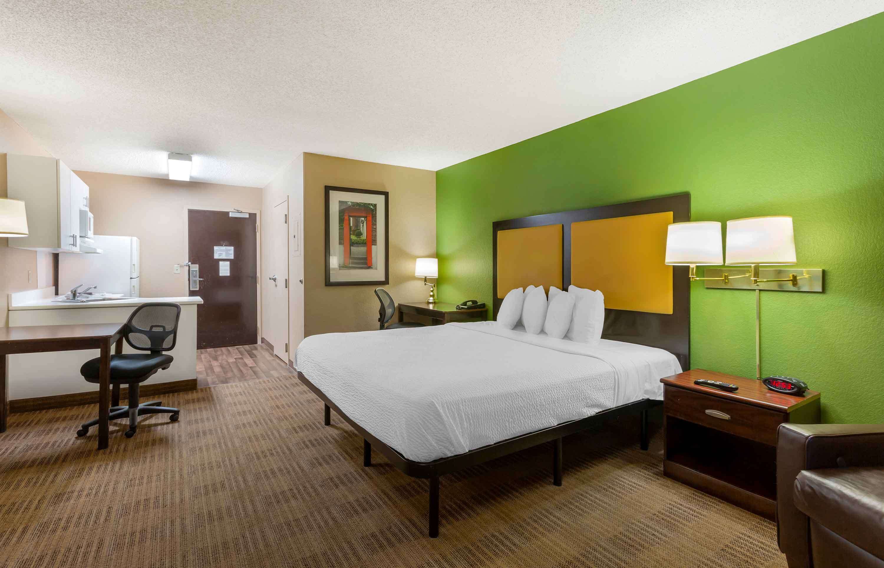A hotel room with a bed, desk, chair, and a green accent wall.