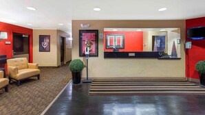Een hotel receptie met een kleurenschema in rood en beige, een receptiebalie, een zithoek met stoelen en een kleine potplant.