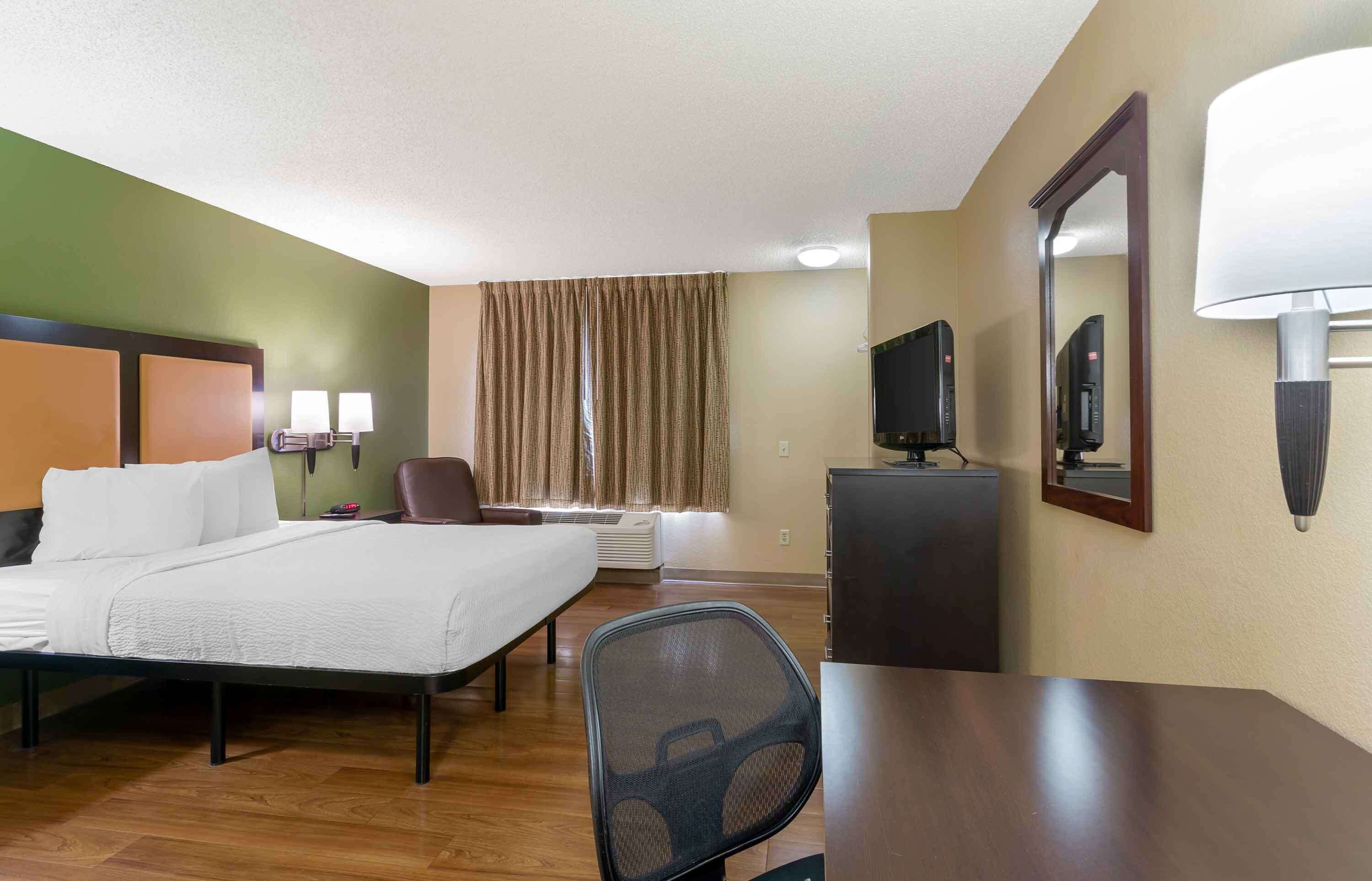 Une chambre d’hôtel avec un lit, un bureau, une chaise, une télévision et un miroir.