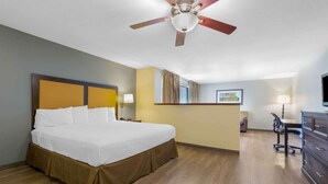 Een hotelkamer met een groot bed, een bureau, een stoel, een plafondventilator en een televisie.
