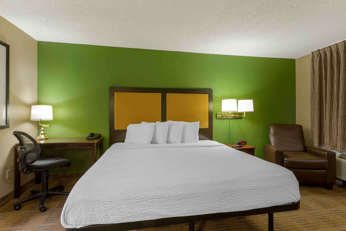 Une chambre d’hôtel avec un grand lit, deux lampes de chevet, un bureau avec une lampe, une chaise et une fenêtre avec des rideaux.