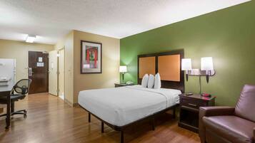A hotel room with a bed, a desk, a chair, a nightstand, and a lamp.