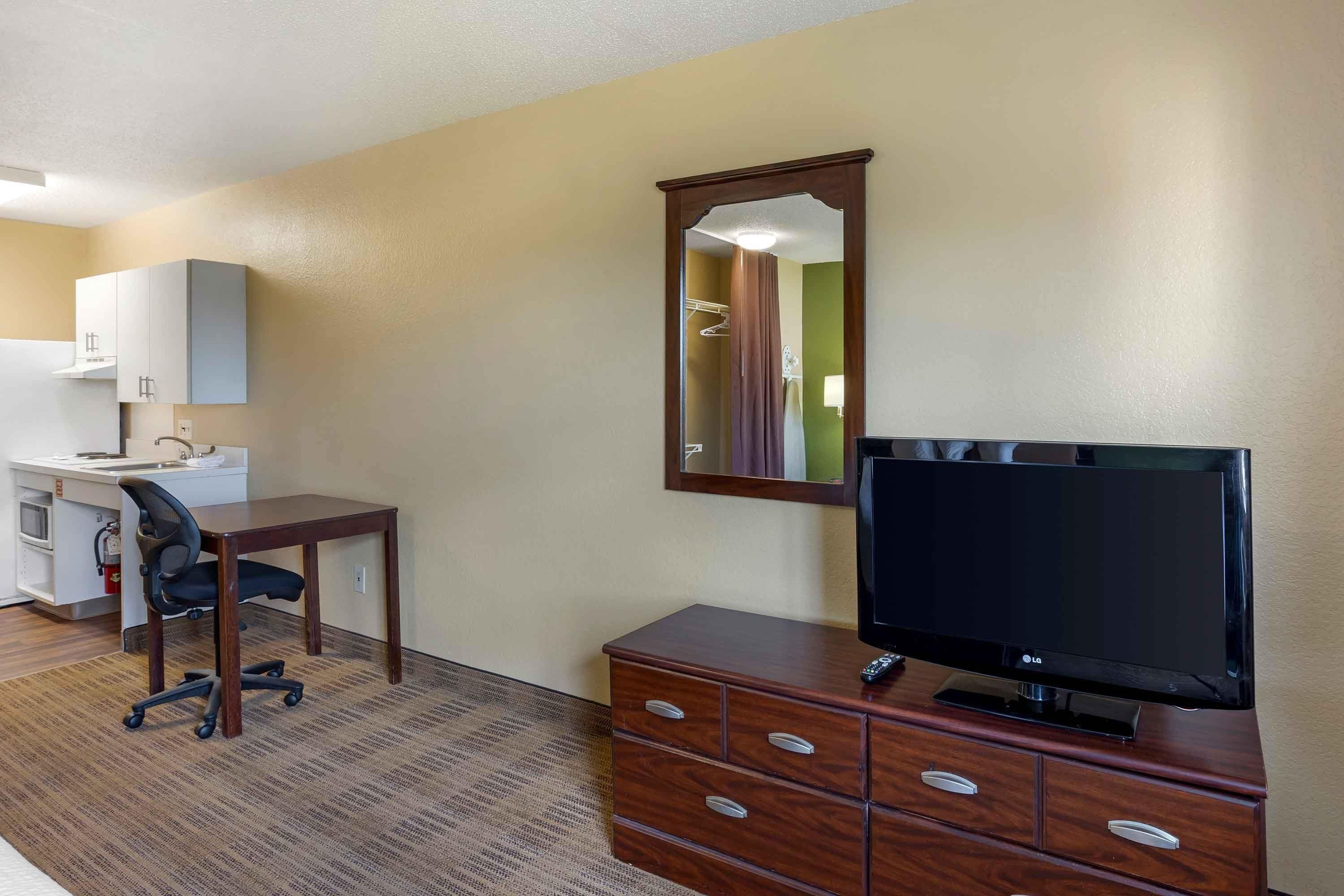 A hotel room with a desk, chair, TV, dresser, and a mirror.