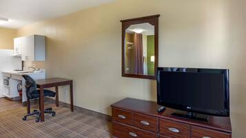 A hotel room with a desk, chair, TV, dresser, and a mirror.
