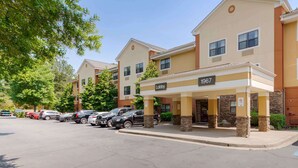 A hotel with a lobby entrance, numbered 1967, and a parking lot with several cars.