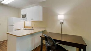 A compact kitchen with white cabinets, a microwave, a refrigerator, a sink, and a small dining area with a chair.