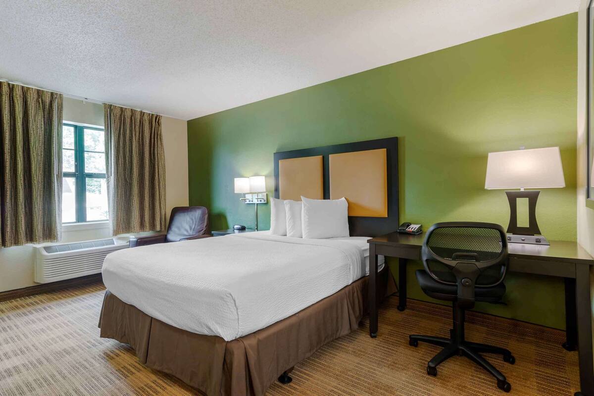 Een hotelkamer met een groot bed, een bureau met stoel, een lamp en een raam met gordijnen.