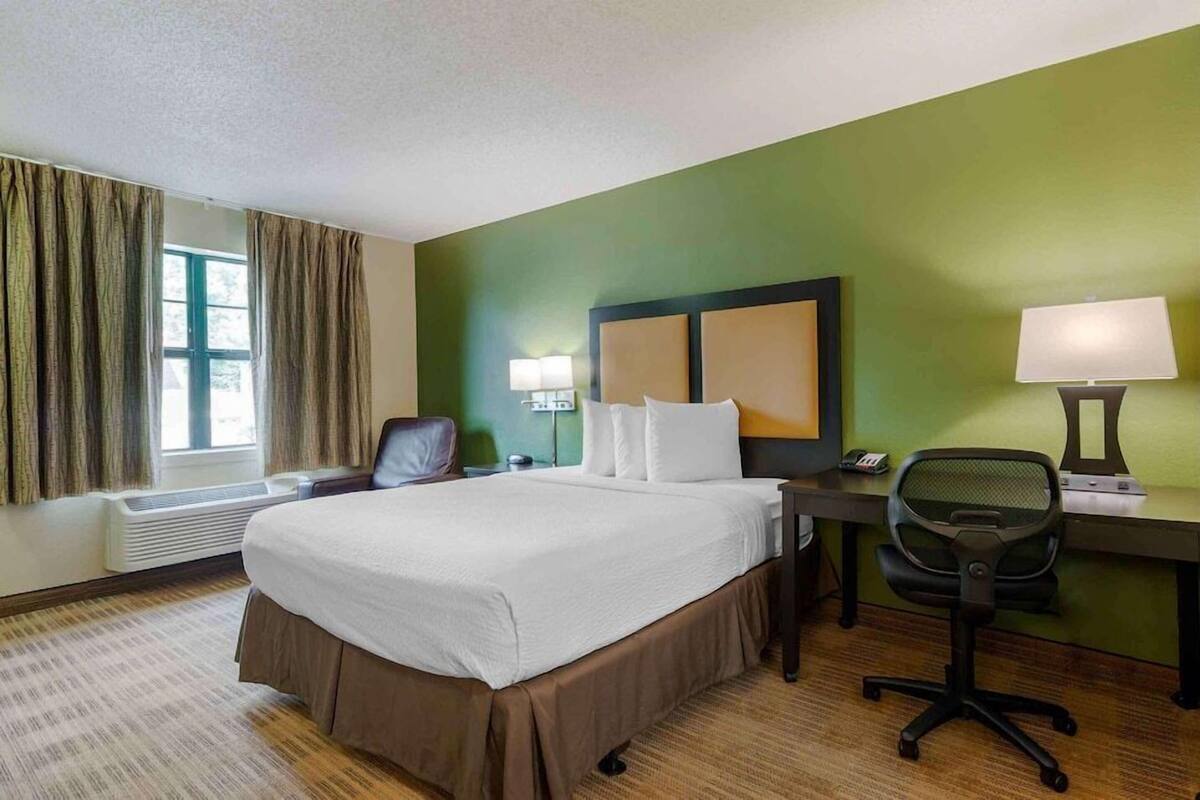 Een hotelkamer met een groot bed, een bureau met stoel, een lamp en een raam met gordijnen.