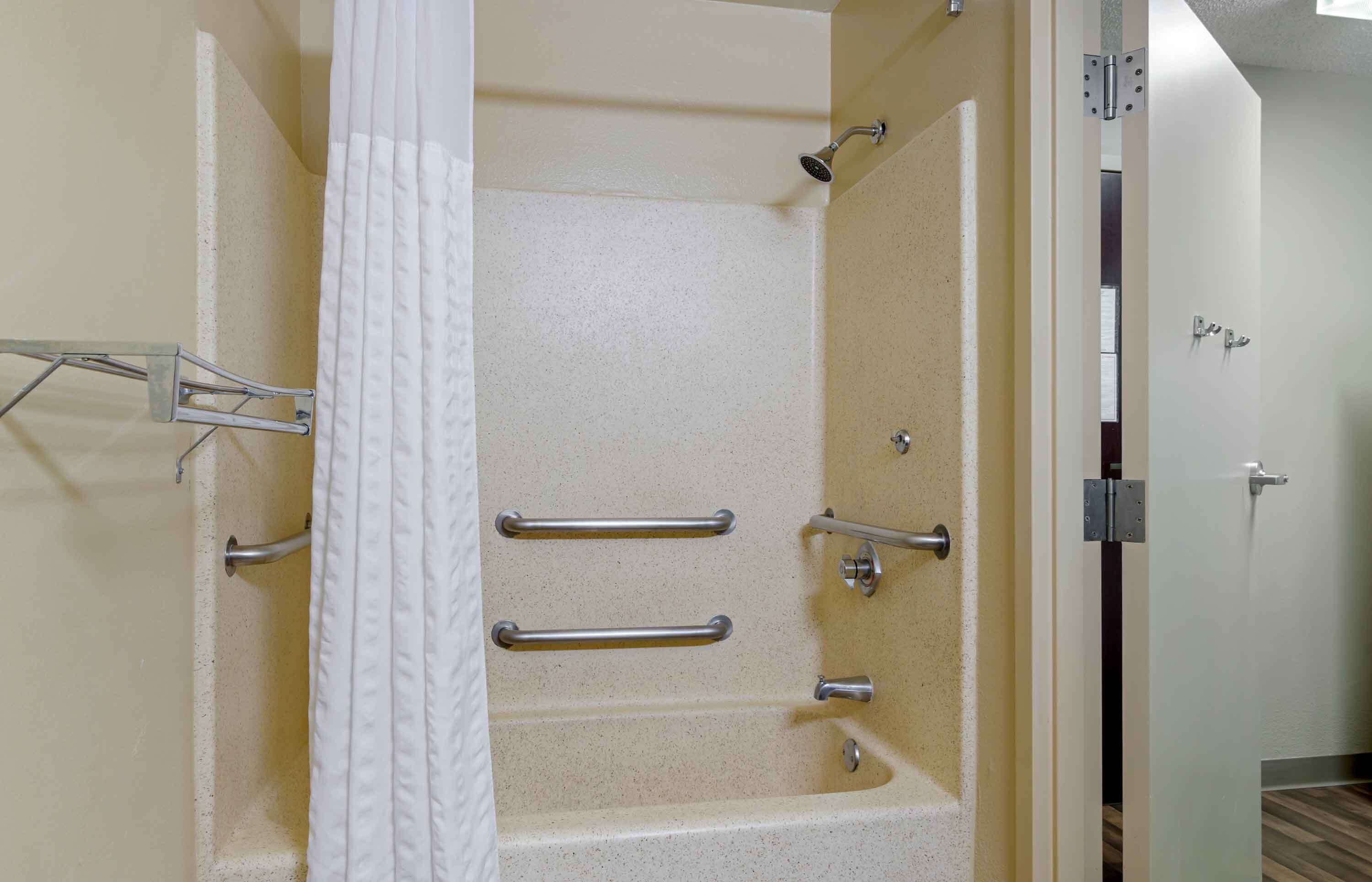 A shower with grab bars, a white curtain, and a door with a handle.