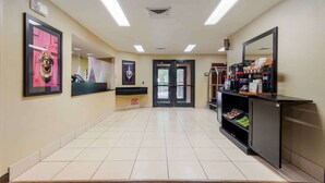 A hotel corridor with a reception desk, framed artwork, a coffee machine, and a trash bin.