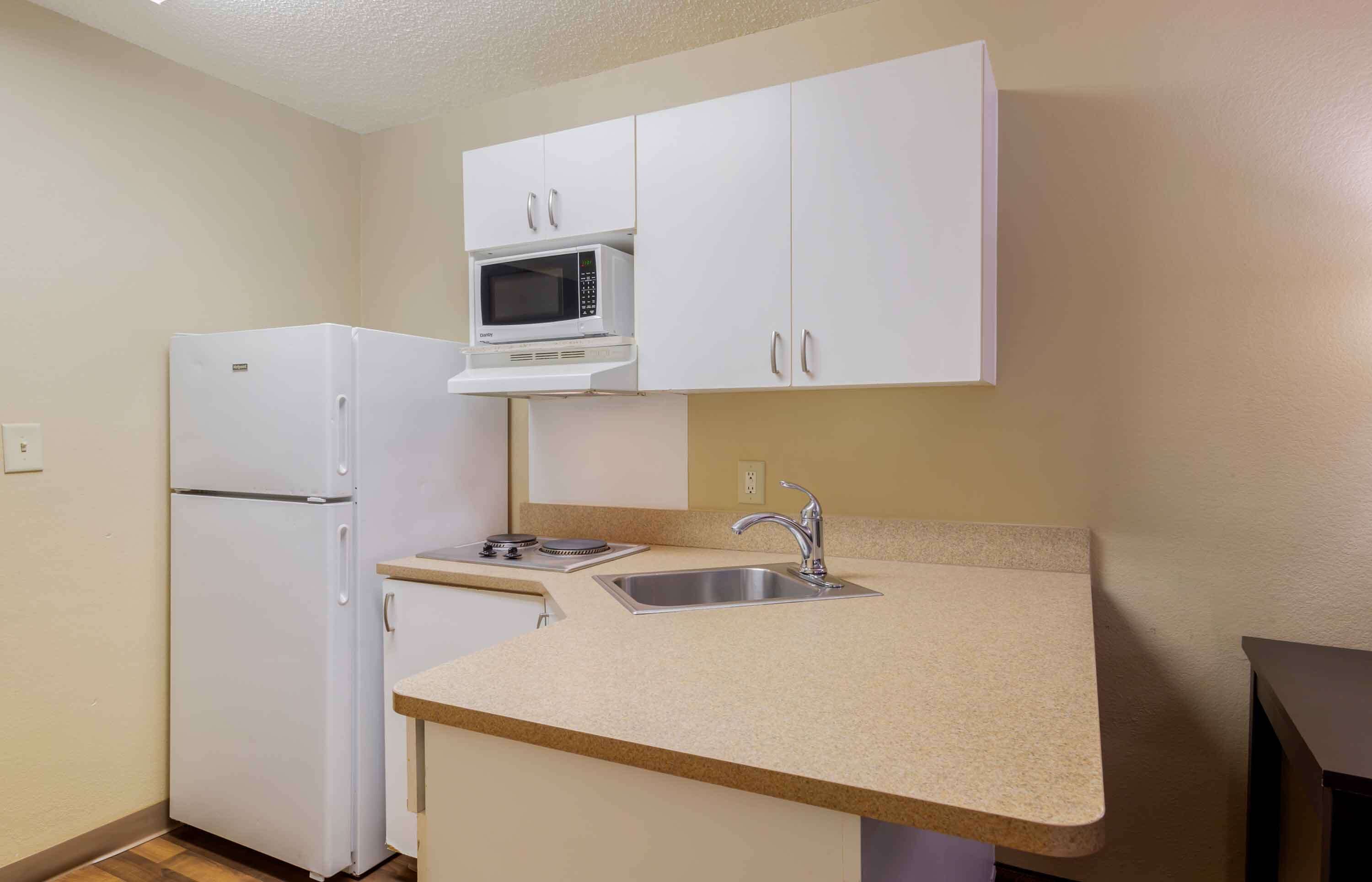 A compact kitchen with white cabinets, a built-in microwave, a stainless steel sink, and a refrigerator.