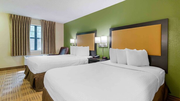 A hotel room with two beds, a window with curtains, a chair, and a nightstand with lamps.