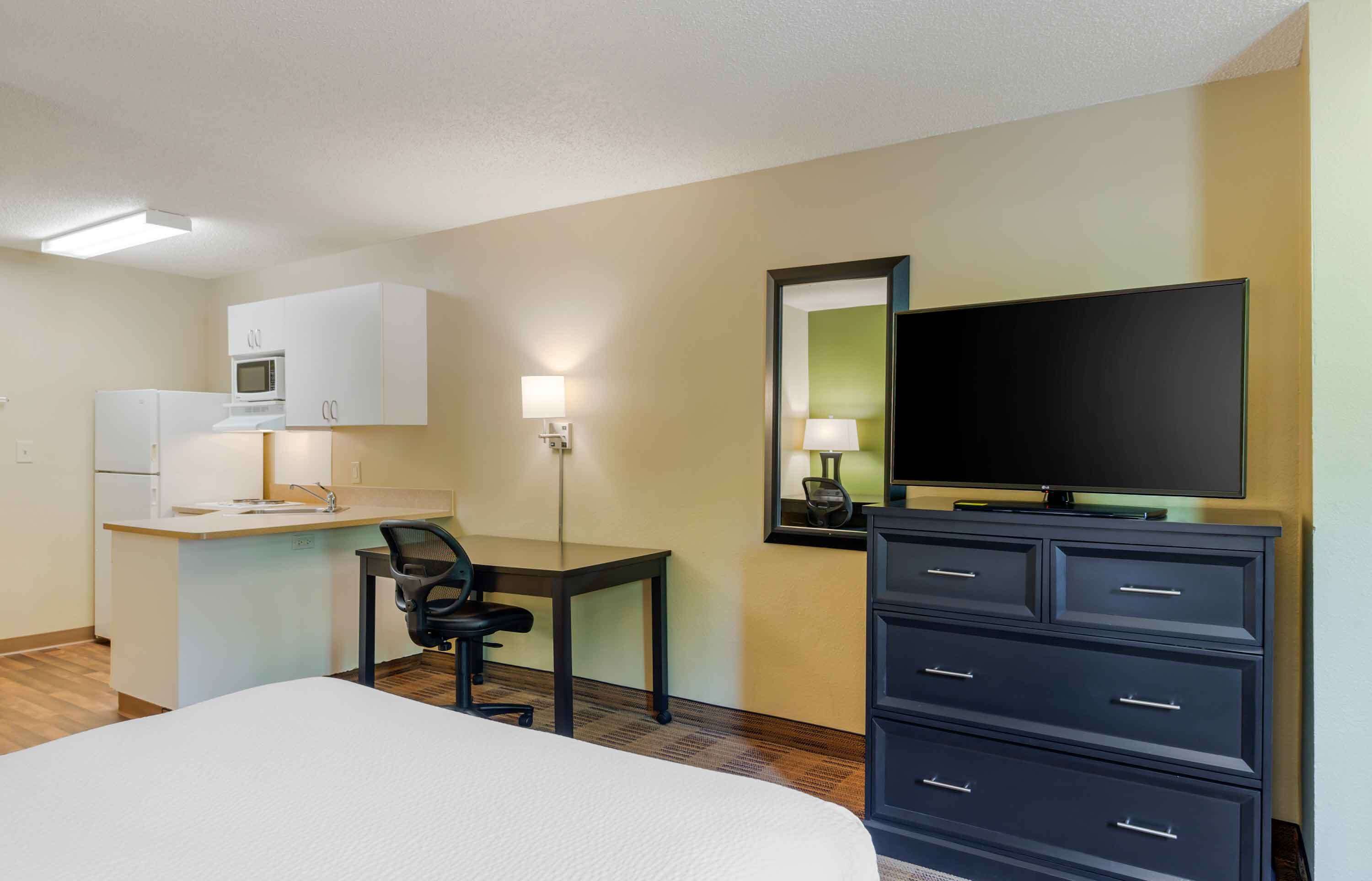A hotel room with a bed, a desk with a chair, a microwave, a TV, and a dresser.