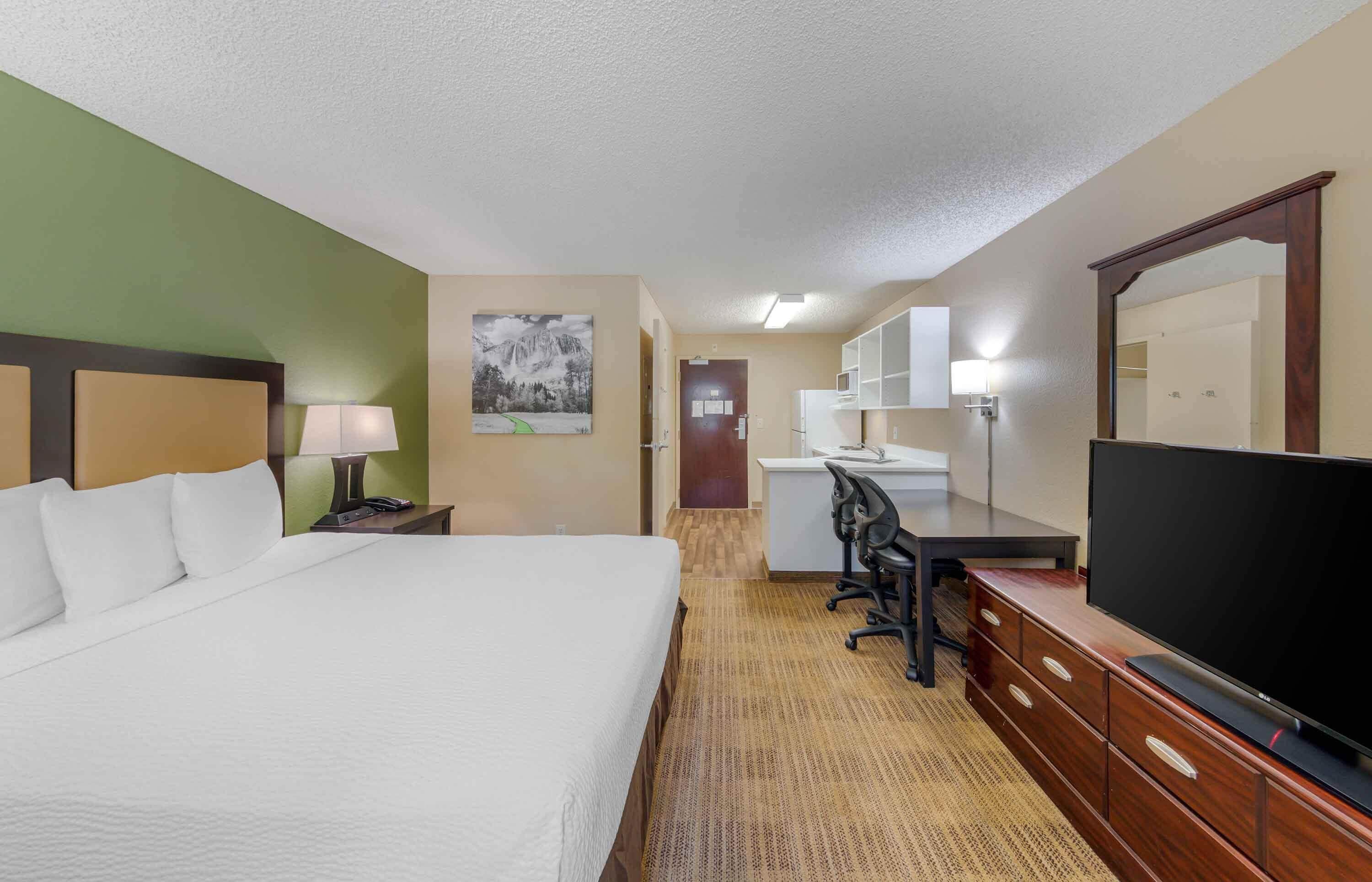 A hotel room with a bed, desk, television, and a mirror.