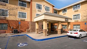 A multi-story hotel with a covered entrance labeled "Lobby," a parking lot with a handicapped parking space, and a white car parked in the lot.