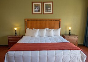 A neatly made bed with white bedding and a red blanket, flanked by two nightstands with lamps, in a room with a wooden headboard and two framed pictures on the wall.