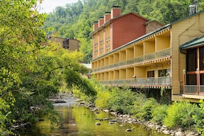 Ein Hotel mit gelber Fassade, einem Balkon mit Metallgeländer und einem Fluss im Vordergrund.