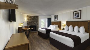 Ein Hotelzimmer mit zwei Betten, einem Holztisch, einem Steinkamin und einem an der Wand befestigten Fernseher.