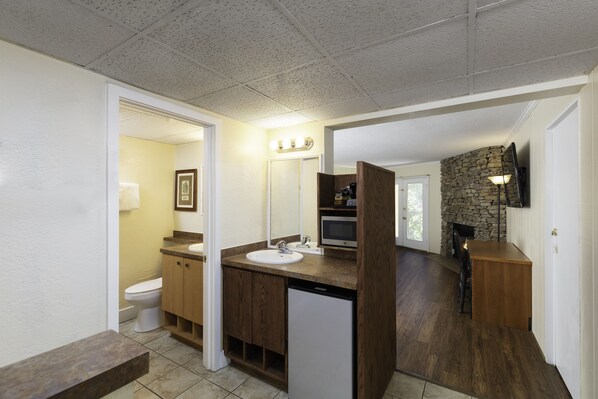 A bathroom with a wooden vanity, a white sink, a toilet, and a stone fireplace.