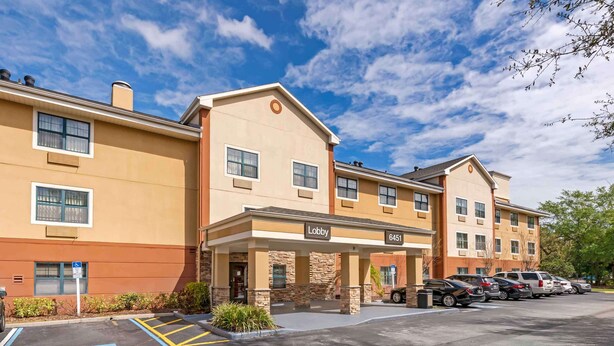 A multi-story hotel with a beige exterior, a lobby entrance, and a parking lot with marked handicapped spaces. - Extended Stay America Select Suites - Orlando - Conven Ctr - Sports Complex (Orlando)