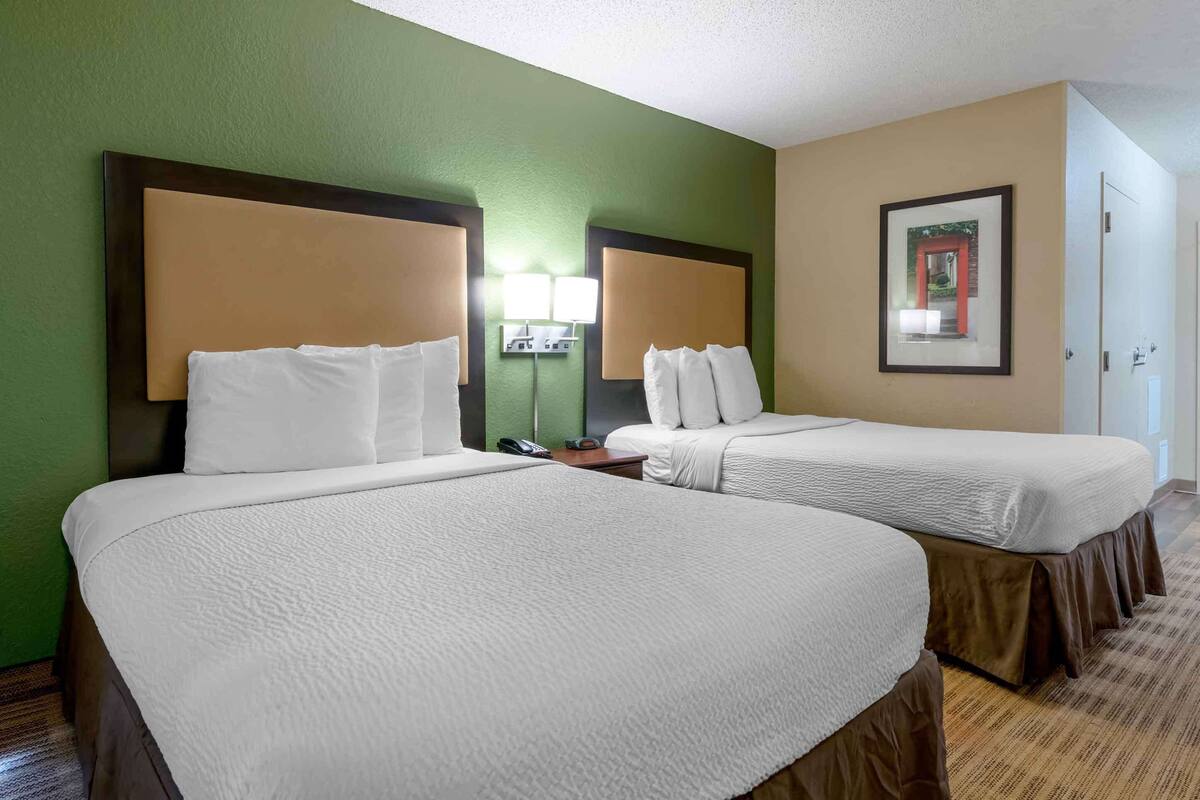 A hotel room with two beds, a nightstand, a lamp, and a framed picture on the wall.