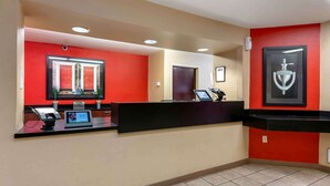 A hotel reception area with a red wall, a black reception desk, and a framed trophy on the wall. - Extended Stay America Select Suites - Orlando - Conven Ctr - Sports Complex (Orlando)