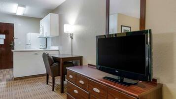 Ein kompaktes Hotelzimmer mit Küchenzeile, einem Flachbildfernseher auf einer Holzkommode, einem Esstisch mit einem Stuhl und einem großen Spiegel an der Wand.
