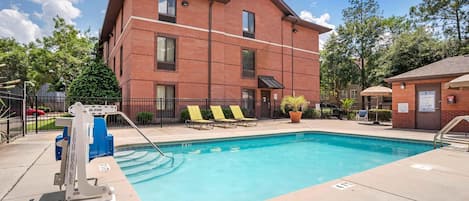 A swimming pool with a lifeguard stand, lounge chairs, and a brick building in the background.