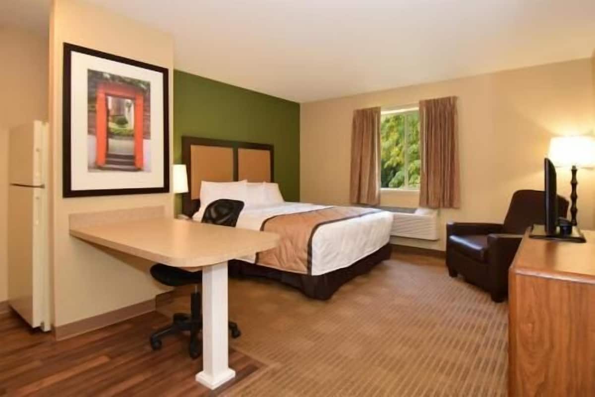 Ein Hotelzimmer mit Bett, Schreibtisch, Stuhl und einem Fenster mit Vorhängen.