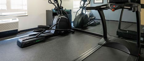A gym with treadmills, elliptical machines, and a mirrored wall.