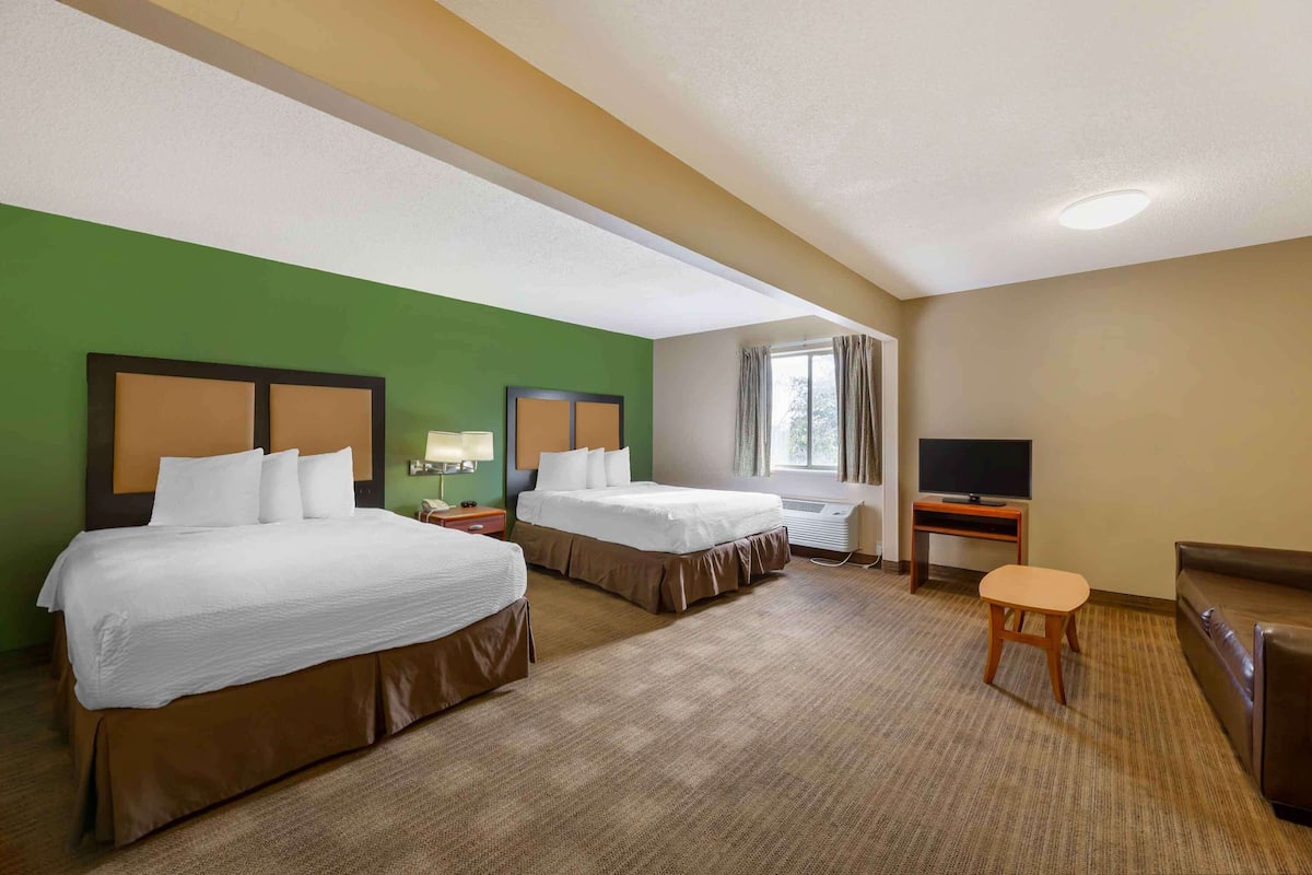 Ein Hotelzimmer mit zwei Betten, einem Fernseher, einem Schreibtisch und einem Fenster.