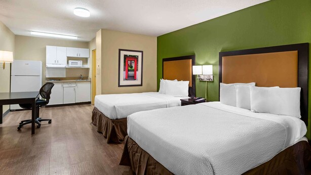 A hotel room with two beds, a desk, a kitchenette, and a green accent wall. - Extended Stay America Suites Richmond W Broad St Glenside S (Richmond)
