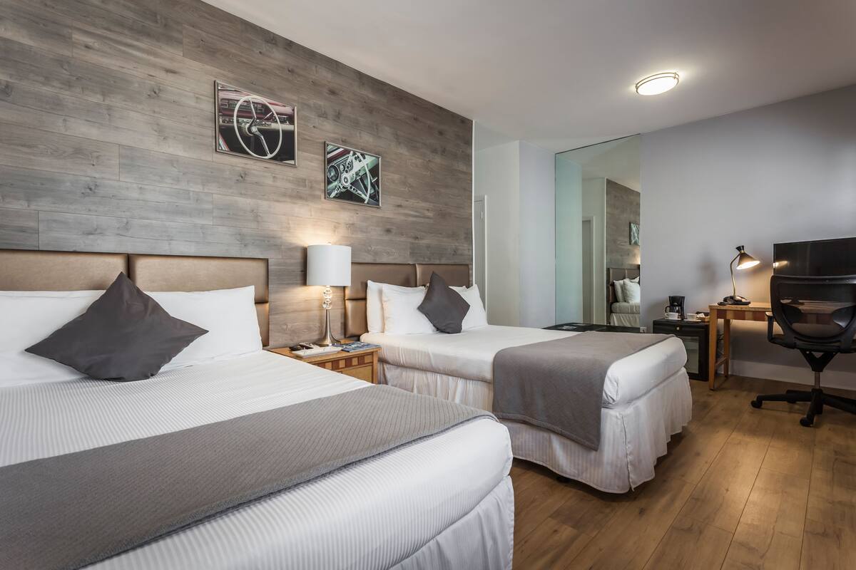 A hotel room with two beds, wooden flooring, a TV, a desk, and a mirror.
