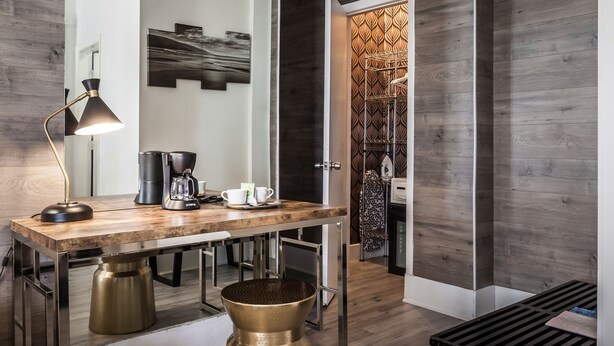 A modern interior with a wooden floor, a large mirror, a coffee station, and a patterned wall. - Century Hotel (Miami Beach)