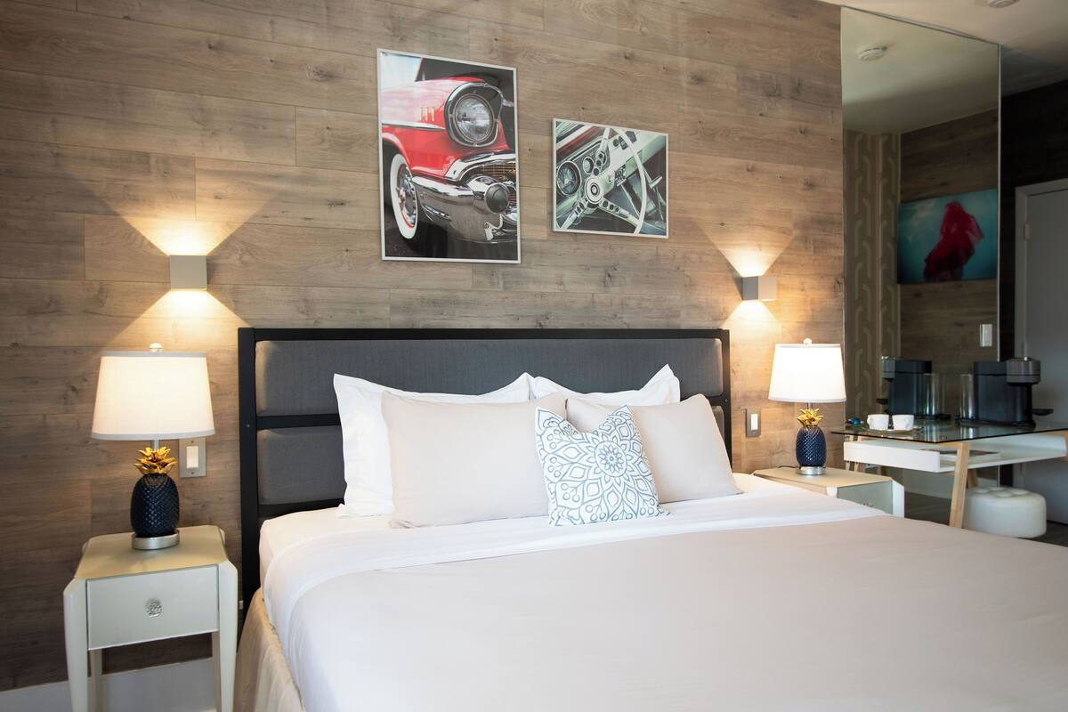 A hotel room with a wooden wall, a bed with white bedding, two nightstands with lamps, and a mirror.