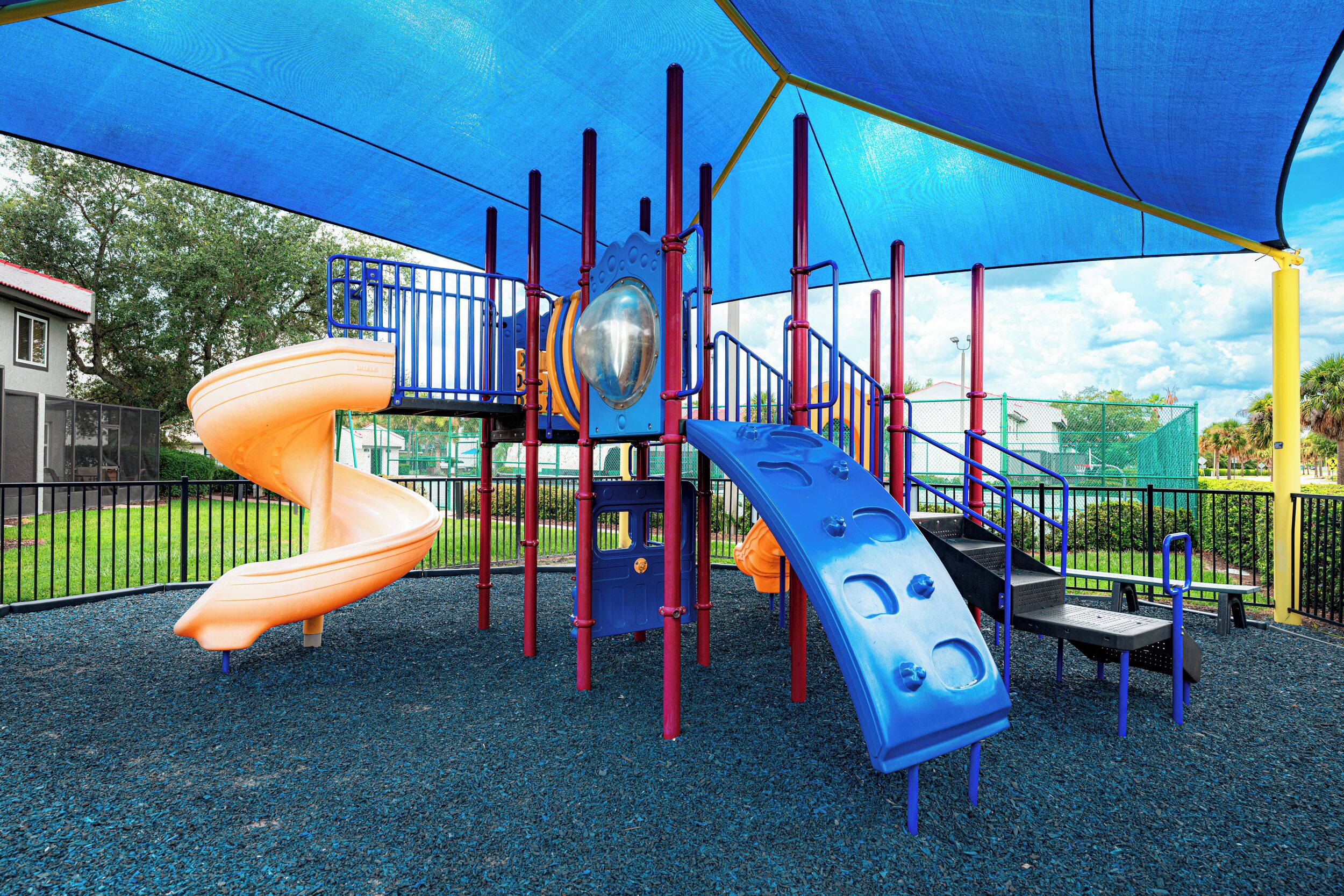 A playground with a slide, climbing structures, and a shaded area.