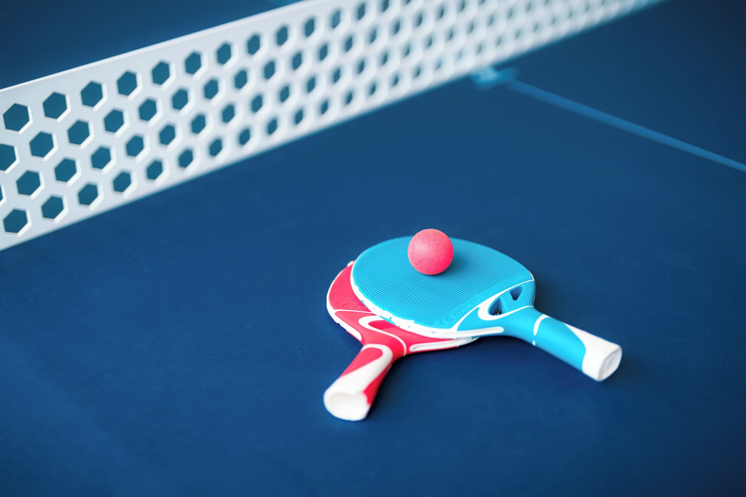A blue and red table tennis table with a net and a ball.