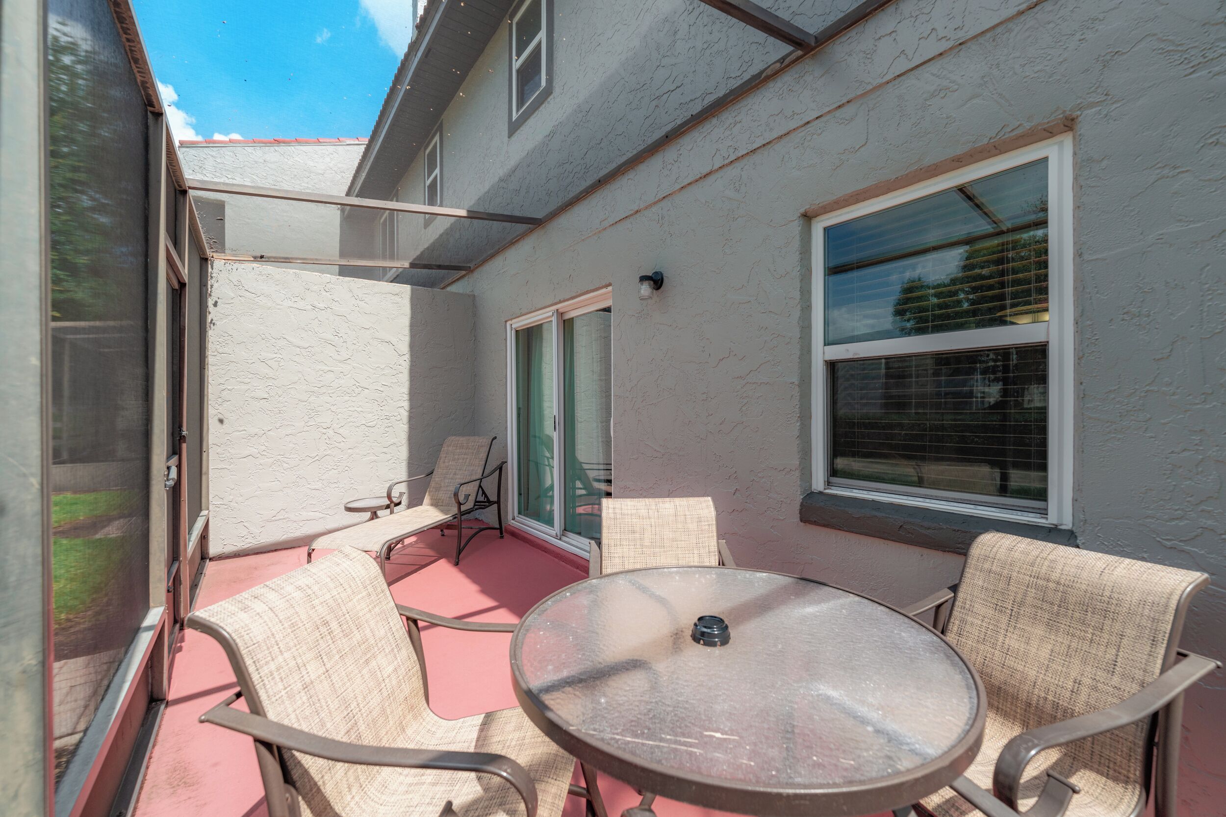 A patio with a round table and four chairs, a sliding glass door, and a window with blinds.