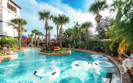 A swimming pool with multiple inflatable rings, surrounded by palm trees and a water slide.