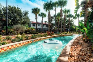 Una piscina con un flotador, rodeada de palmeras y un edificio al fondo.