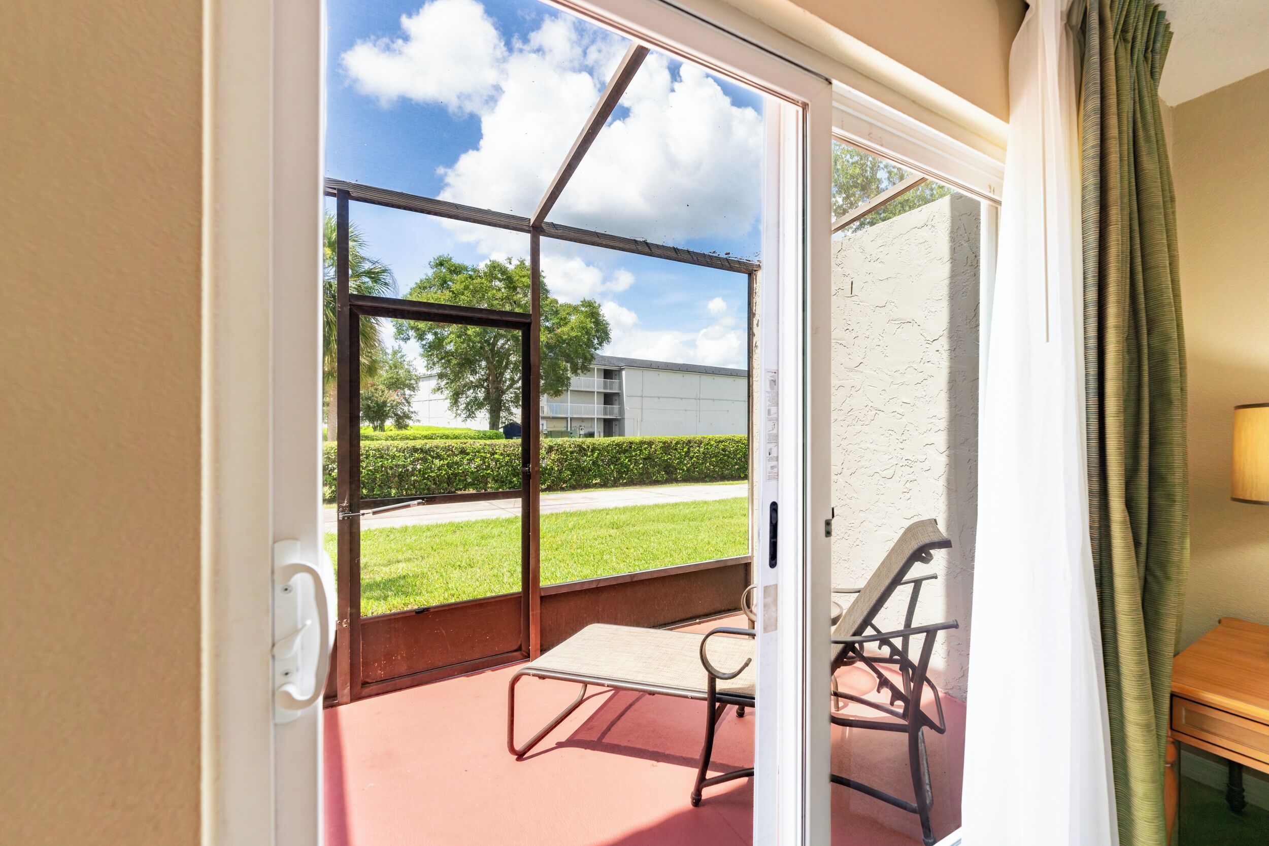 A room with a sliding glass door leading to an outdoor patio. The patio has a red floor and includes a metal chair and a small table.