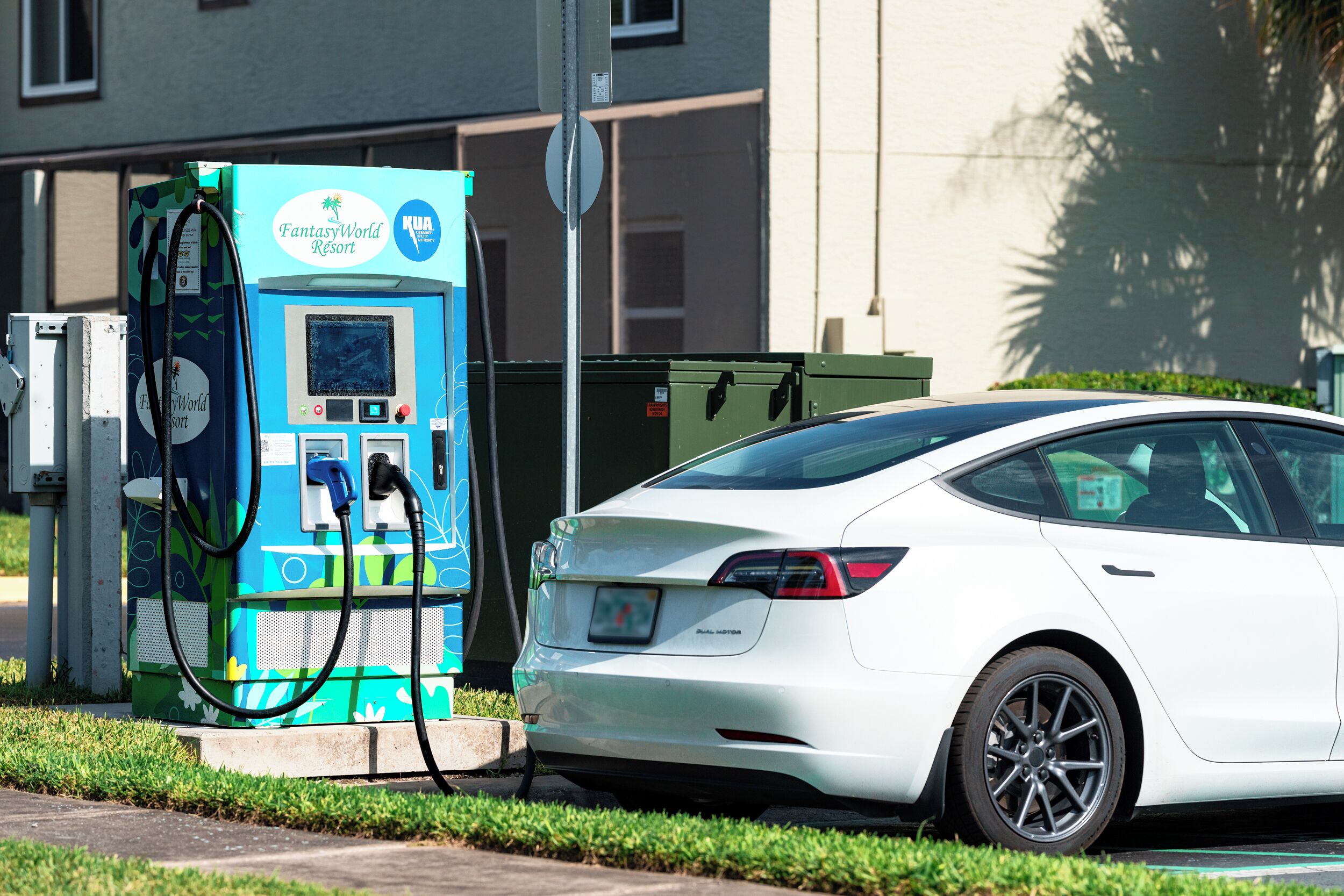 A white car parked at an electric charging station with a FantasyWorld Resort sign.