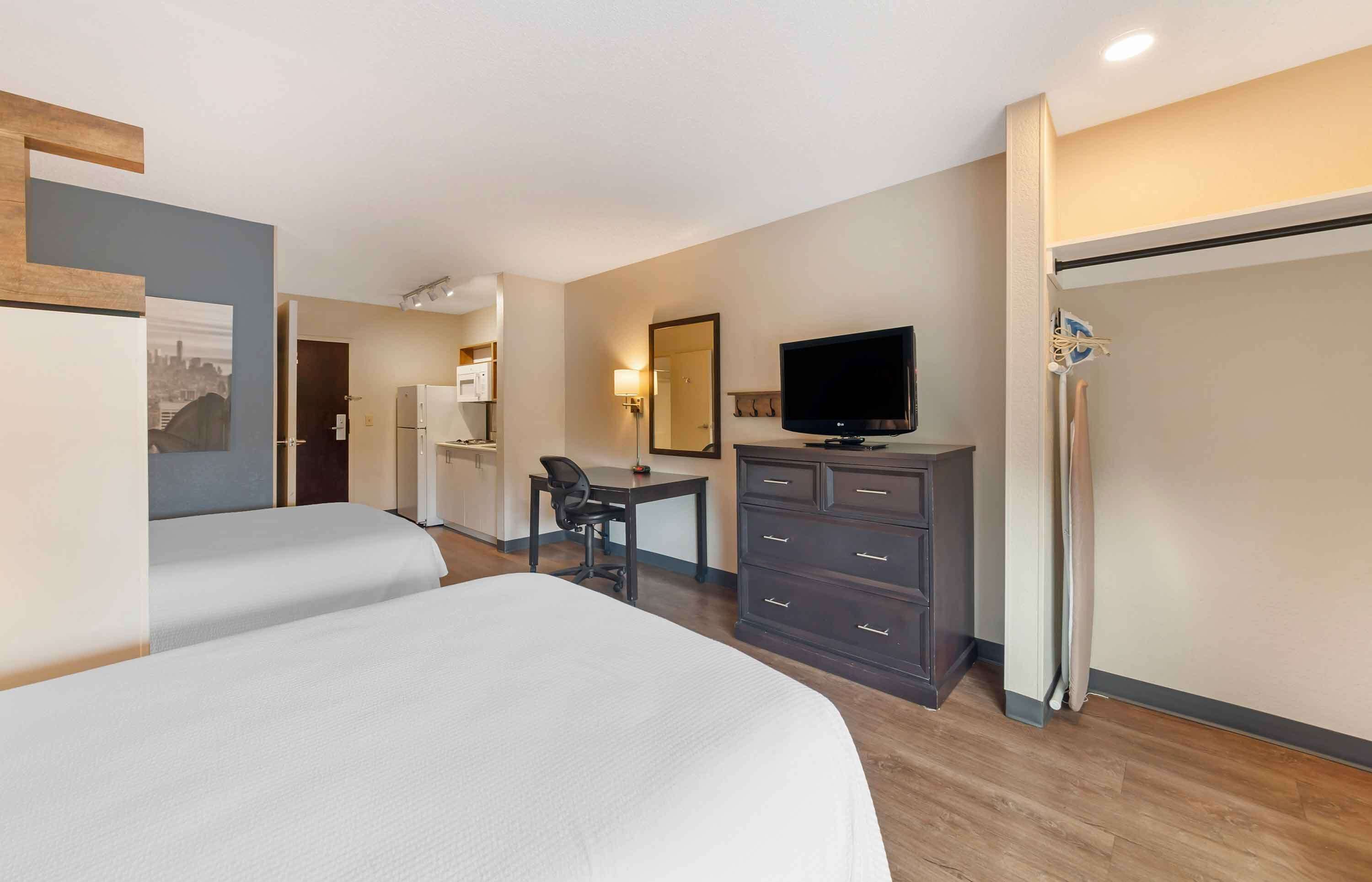 A hotel room with two beds, a desk, a television, a wardrobe, and a mirror.