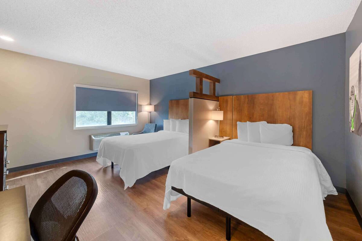 Ein Hotelzimmer mit zwei Betten, einem Schreibtisch, einem Stuhl und einem Fenster.