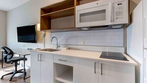 Une cuisine compacte avec des meubles blancs, un four à micro-ondes, un évier et un téléviseur à écran plat.